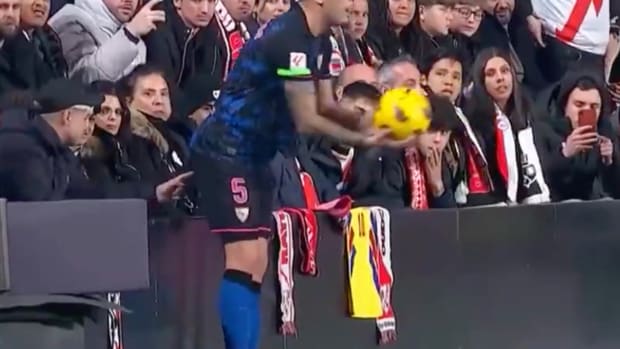 Sevilla's Lucas Ocampos pictured preparing to take a throw-in during a La Liga game against Rayo Vallecano as a fan wearing a baseball cap in the front row appears to poke the player's butt with his index finger