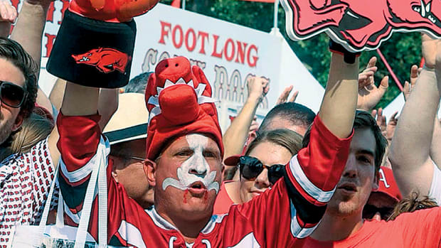 An Arkansas fan heavily adorned in Razorback gear with tusks painted on his face calls the Hogs outside the stadium before a football game.