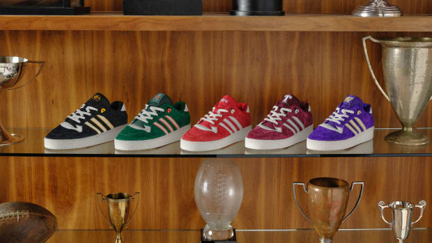 Adidas Rivalry sneakers in college colors sit on a trophy case.
