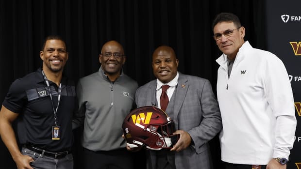 Eric Bieniemy (holding helmet) poses with (L-R) Washington Commanders team president Jason Wright, general manager Martin Mayhew, and head coach Ron Rivera.