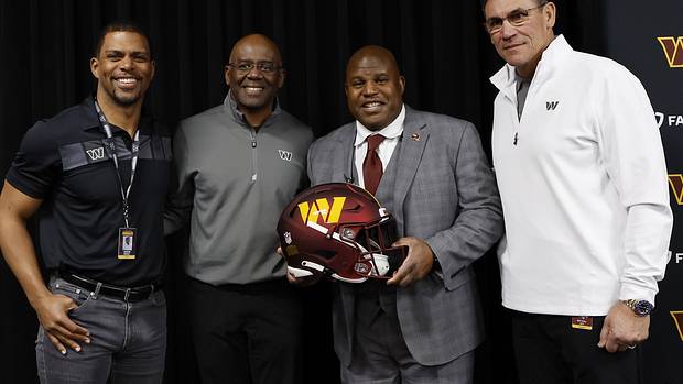 Eric Bieniemy (holding helmet) poses with (L-R) Washington Commanders team president Jason Wright, general manager Martin Mayhew, and head coach Ron Rivera.