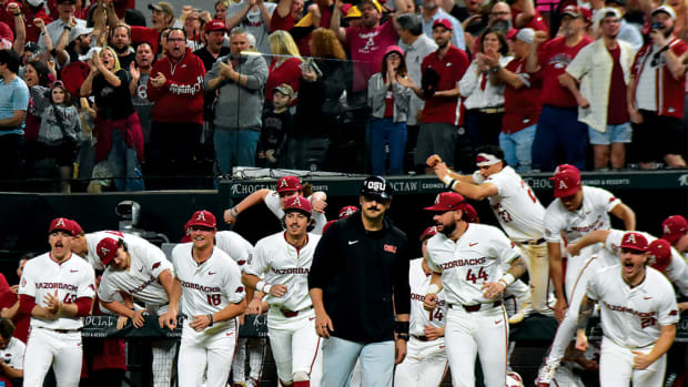 The Razorbacks rush the field after the final out of a win over Oregon State at Globe Life Field while a packed Arkansas crowd cheers behind them.
