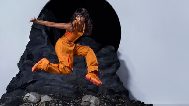 Woman wearing orange adidas clothing jumping in photo shoot.