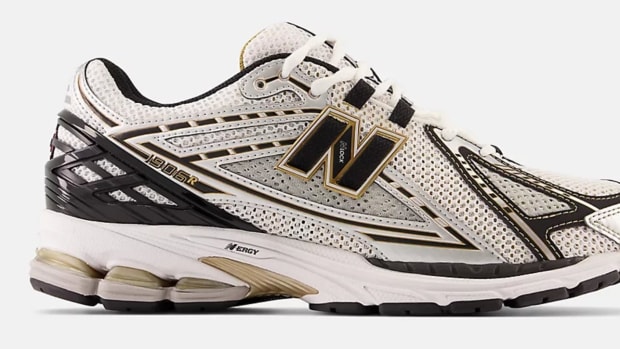 Side view of a white, black, and gold New Balance shoe.