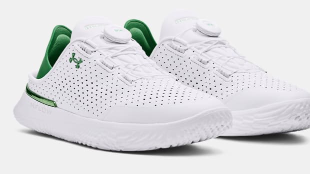 Side view of white and green Under Armour shoes.