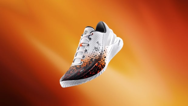 View of white, black, and orange Under Armour shoes.