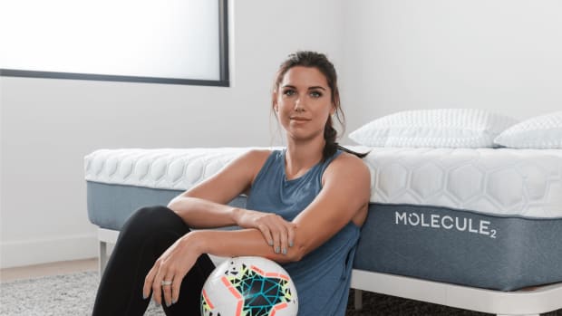 Alex Morgan poses with a soccer ball next to a bed.