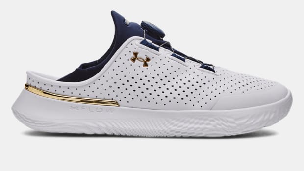 Side view of a white and navy Under Armour shoe.