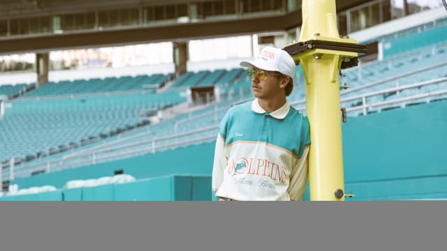 A man models Miami Dolphins apparel on a football field.