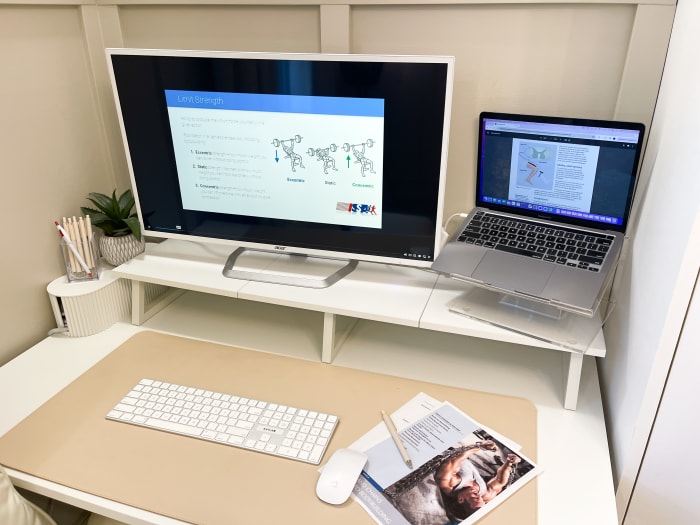 laptop and second screen on desk with study materials for ISSA bodybuilding course on screen. paper printouts of study materials and a pencil are on the righthand side of a mouse and keyboard