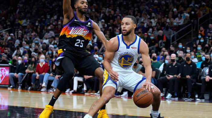 Golden State Warriors point guard Stephen Curry (30) is defended by Phoenix Suns forward Mikal Bridges during the first half of an NBA basketball game on Saturday, Dec. 25, 2021, in Phoenix.