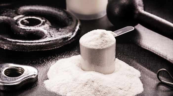 A scoop of white casein protein powder next to metal weight plates