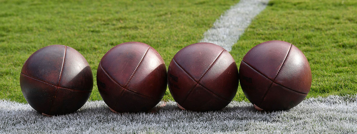 Four unmarked footballs on a grass field