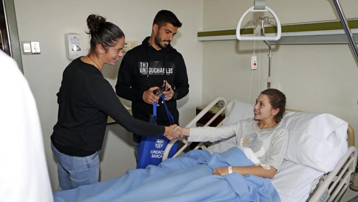 Marta TorrejÃ³n y Luis SuÃ¡rez saludan a una paciente en la visita al Hospital de Barcelona.