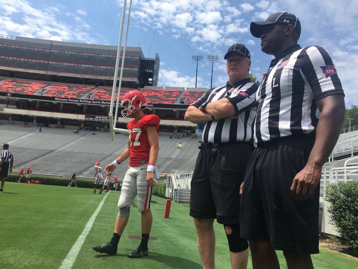 Russ Pulley and Walter Flowers, two SEC officials, talk with one another ahead of Georgia camp scrimmage earlier this month. A UGA specialist is in the background warming up.