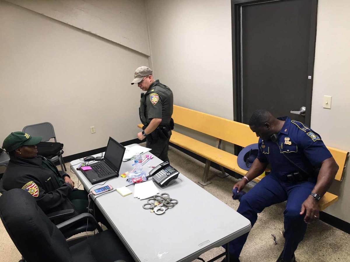 The Processing Room under Tiger Stadium, which houses those who have been ejected from a game. Sheriff deputy Leticia Ware sits at a computer. Deputy Blair Nicholson is standing, and State Police Capt. Anthony Pitts is seated on the bleacher normally reserved for unruly students.