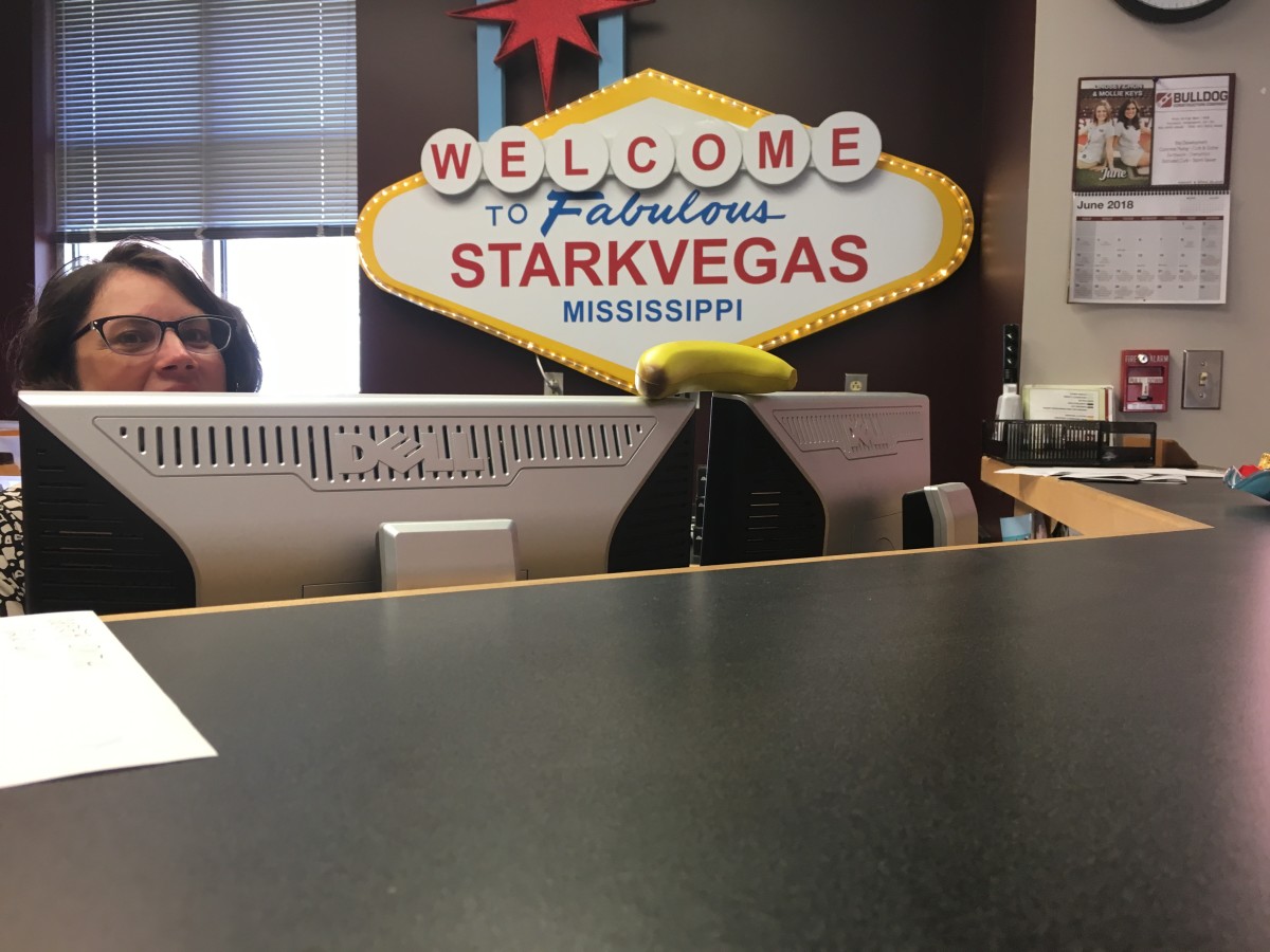 Mississippi State baseball secretary April Edwards peeks from over her computer screen at the banana resting on top of the machines. The Bulldogs have adopted the fruit as a rallying tool this postseason.