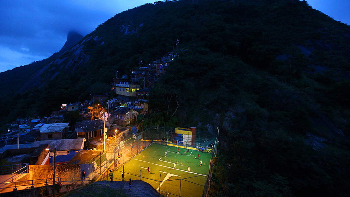 Children play soccer on a field thousands of feet above the Rio from the postcards, a grass area lined with a fence. 