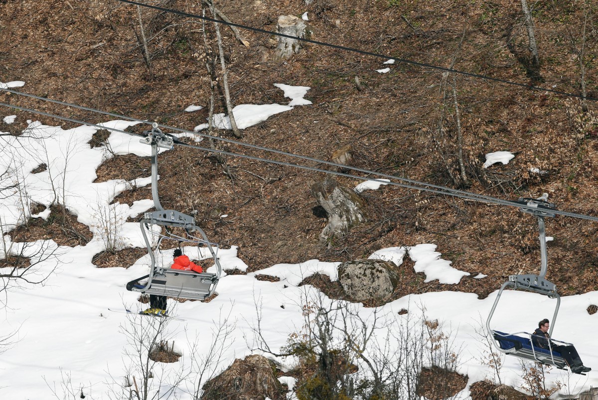 People take a ski lift past patches of snow at the Sochi 2014 Winter Olympics, Tuesday, Feb. 11, 2014, in Krasnaya Polyana, Russia. Warm temperatures in the mountains was a factor in the cancellation of Women's downhill training on Tuesday. (AP Photo/Christophe Ena)