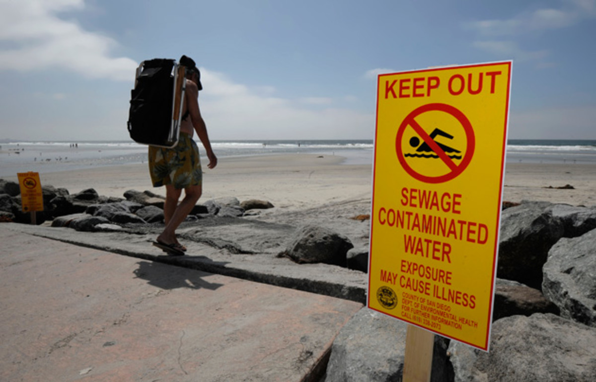 A beachgoer walks past a sign posted to warn people of contaminated water at Torrey Pines State Beach in San Diego. The Heal the Bay Beach Report Card provides a weekly analysis of coastline water quality on the West Coast, over 500 beaches are graded A to F based on bacteria analysis.