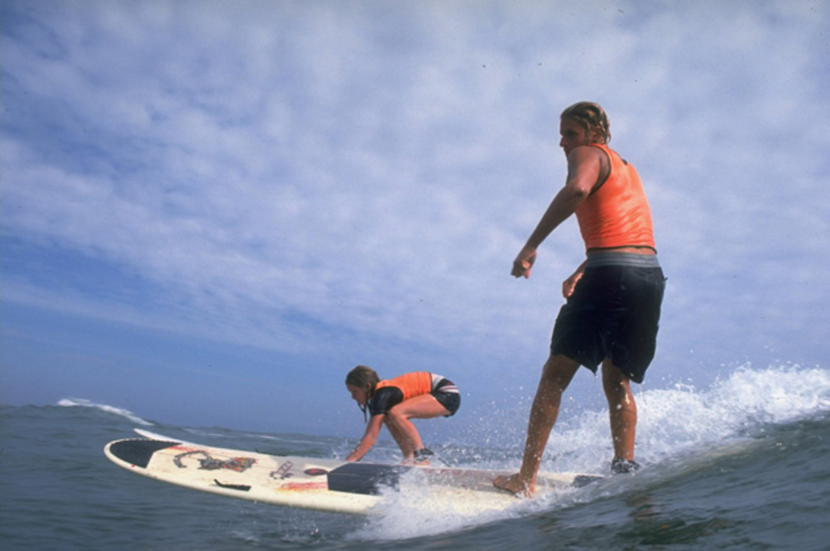 Joshua Paskowitz teaches a camper how to stand on a surf board.