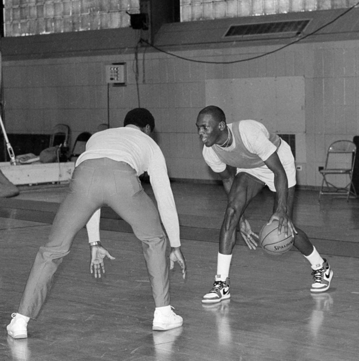 The Chicago Bulls' Michael Jordan looks at assistant coach Fred Carter as he moves the ball between his legs during a team workout in Chicago, 1985.
