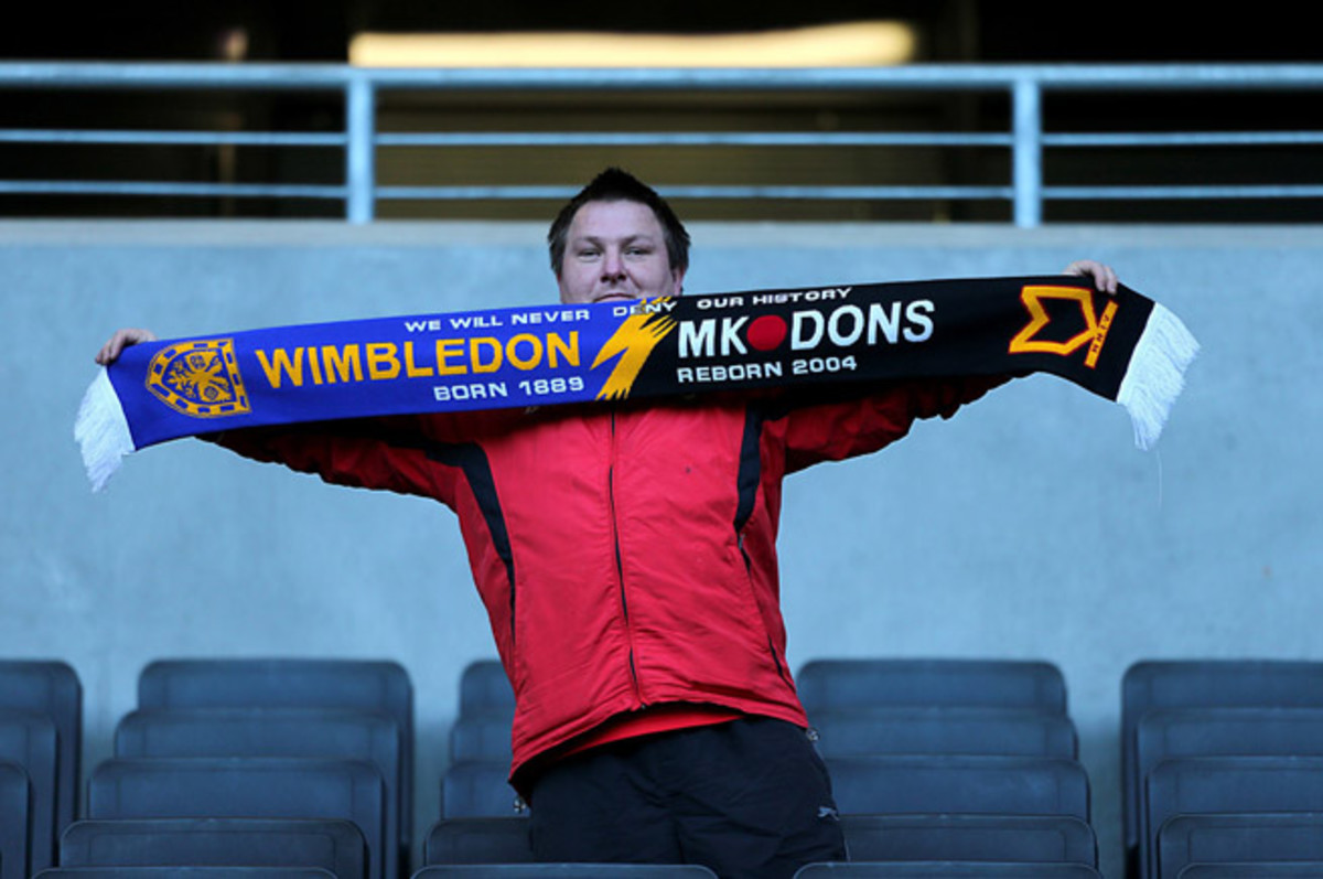 A fan holds a scarf commemorating Wimbledon's FA Cup match against MK Dons in the 2012 FA Cup, an emotional day for Wimbledon supporters confronting their past and present.