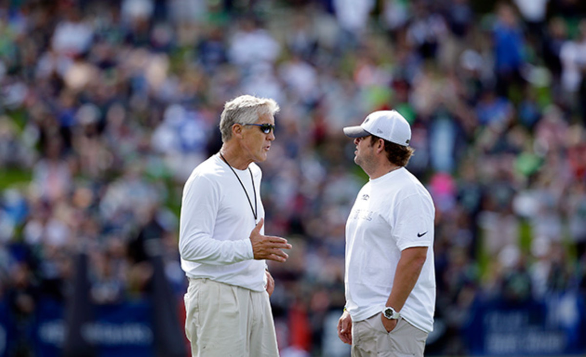 Seattle Seahawks head coach Pete Carroll, left, talks with general manager John Schneider as fans fill a hill behind at an NFL football camp practice Friday, July 25, 2014, in Renton, Wash.