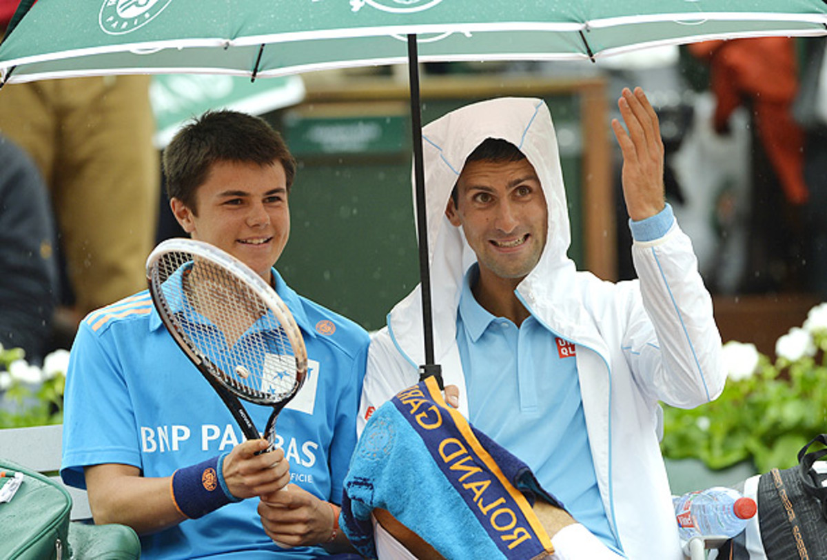 Novak Djokovic shares a seat and an umbrella with a ball boy during his first-round match. (MIGUEL MEDINA/AFP/Getty Images)