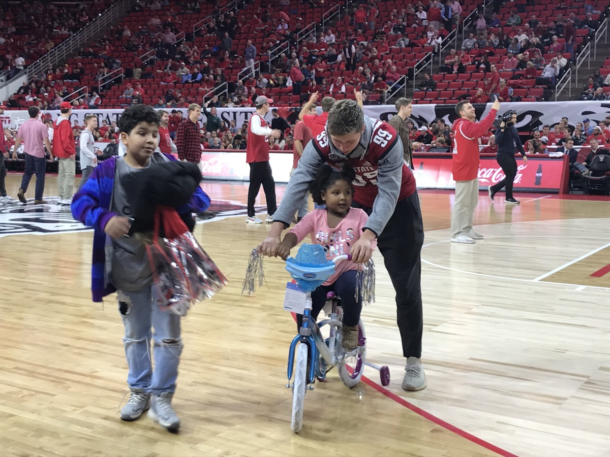 All-ACC punter Trenton Gill helps a young fan ride her new bike at halftime of Wednesday's basketball game