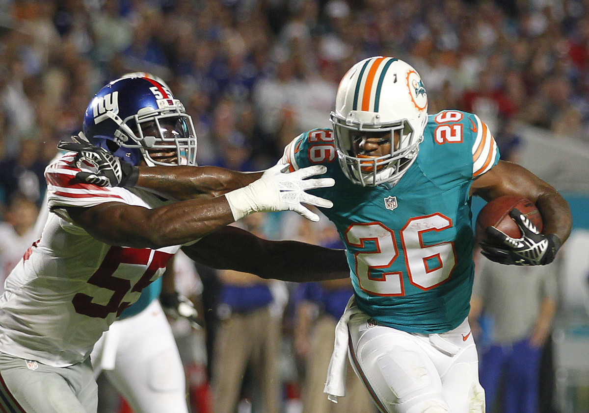 Dolphins running back Lamar Miller (26) stiff arms Giants linebacker, J.T. Thomas, on his way to a touchdown in a 2015 game.