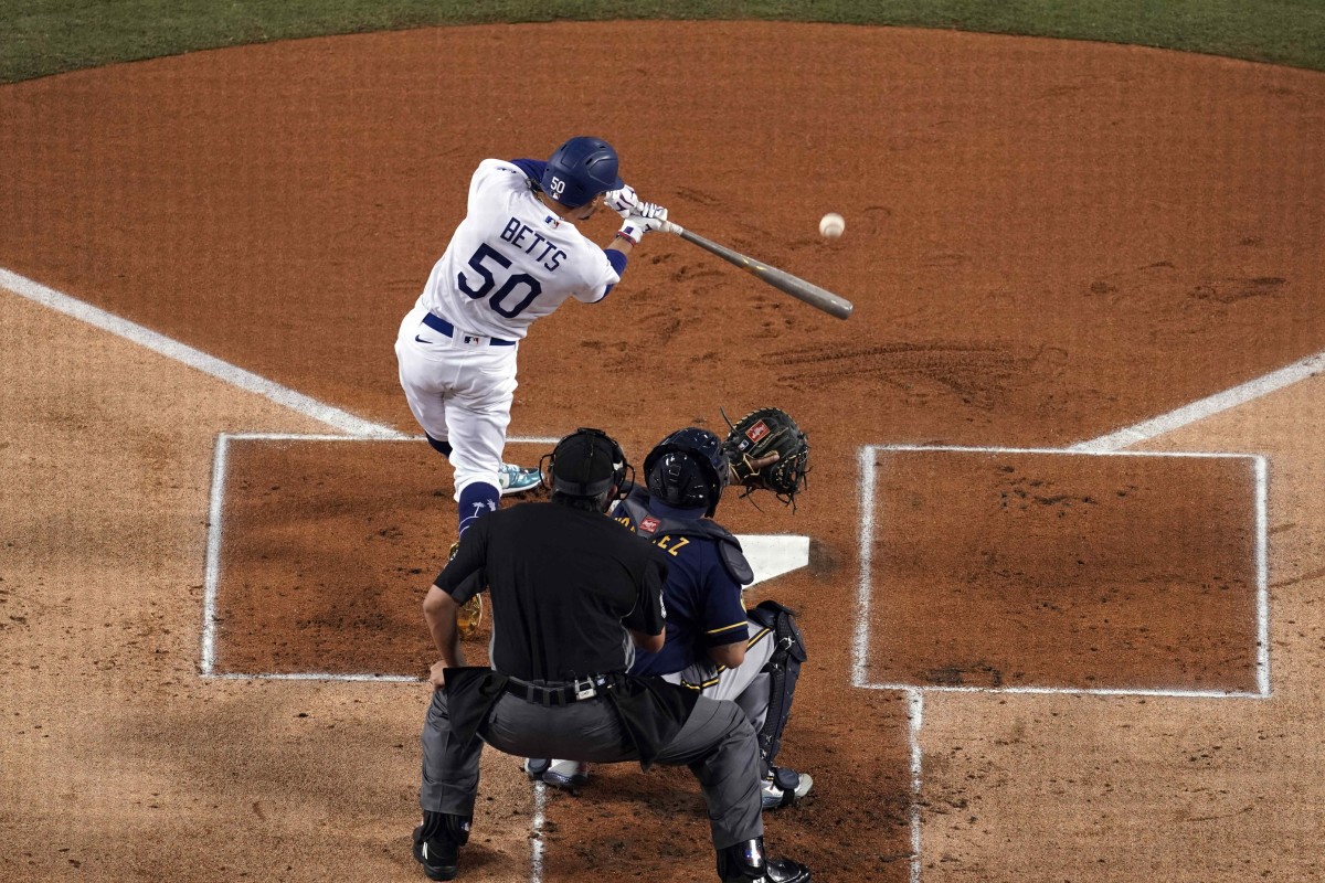 Sep 30, 2020; Los Angeles, California, USA; Los Angeles Dodgers right fielder Mookie Betts (50) follows through on a double in the first inning as Milwaukee Brewers catcher Omar Narvaez (10) and umpire Mark Ripperger (90) watch during Game 1 of the National League Wild Card Playoffs at Dodger Stadium. Mandatory Credit: Kirby Lee-USA TODAY Sports
