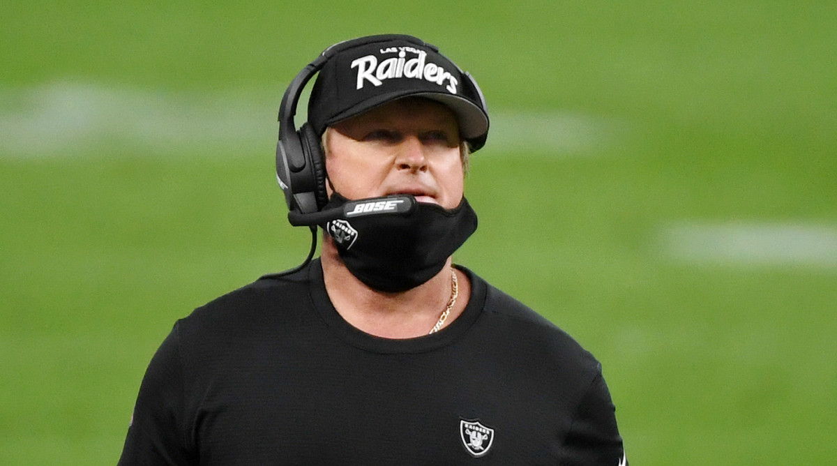 Jon Gruden walks on the sideline with his mask pulled down.