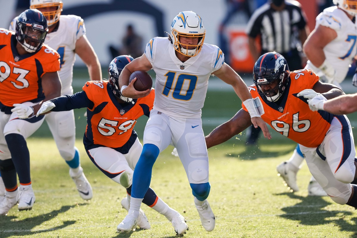 Los Angeles Chargers quarterback Justin Herbert (10) runs the ball as Denver Broncos defensive end Shelby Harris (96) and linebacker Malik Reed (59) defend in the first quarter at Empower Field at Mile High.