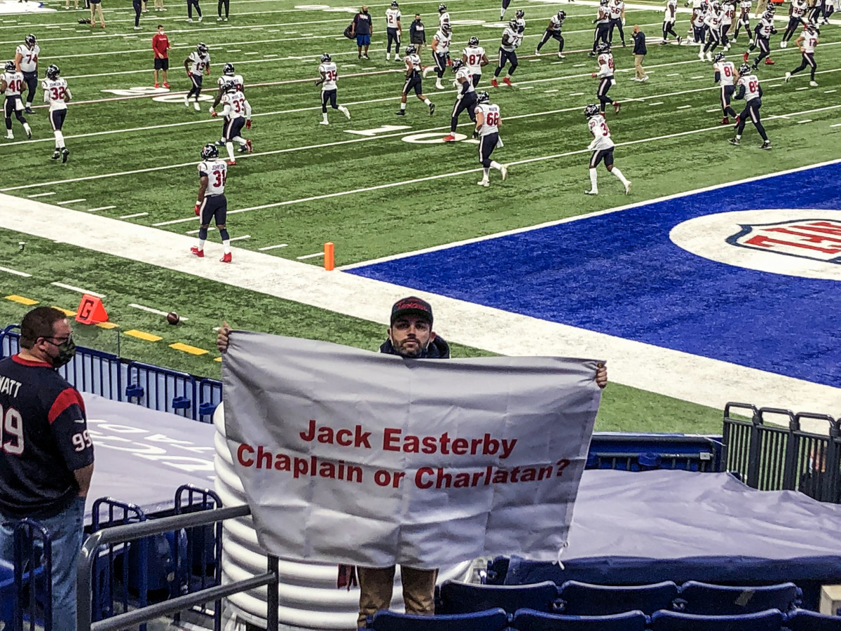 Texans fan Ronnie Baker holds up a sign—"Jack Easterby Chaplain or Charlatan?"—before a Texans-Colts game