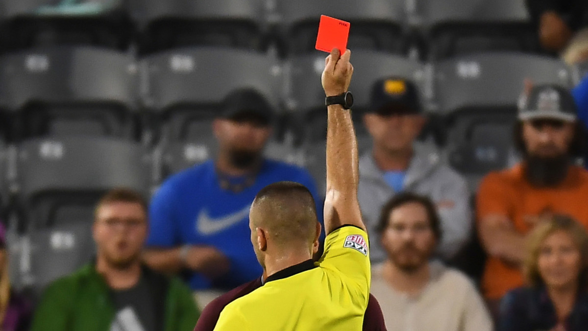 A soccer referee issues a red card, with his back to the camera