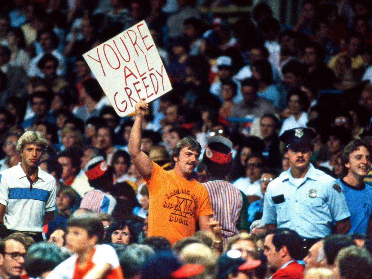 Baseball fan holds up a sign attacking players and owners: "YOU'RE ALL GREEDY"