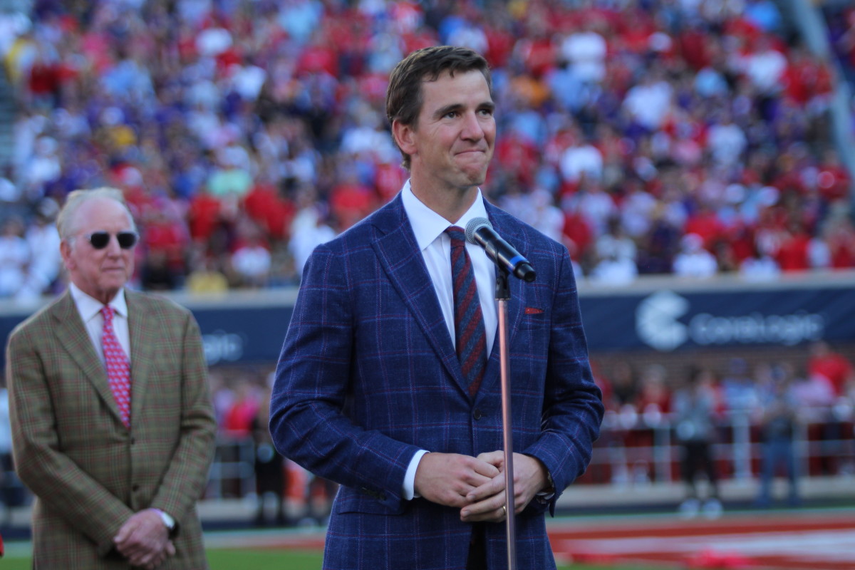 Former Ole Miss quarterback Eli Manning speaks at his jersey retirement ceremony as his father and fellow ex-Rebels signal-caller Archie Manning looks on at Vaught-Hemingway Stadium Oct. 23, 2021.