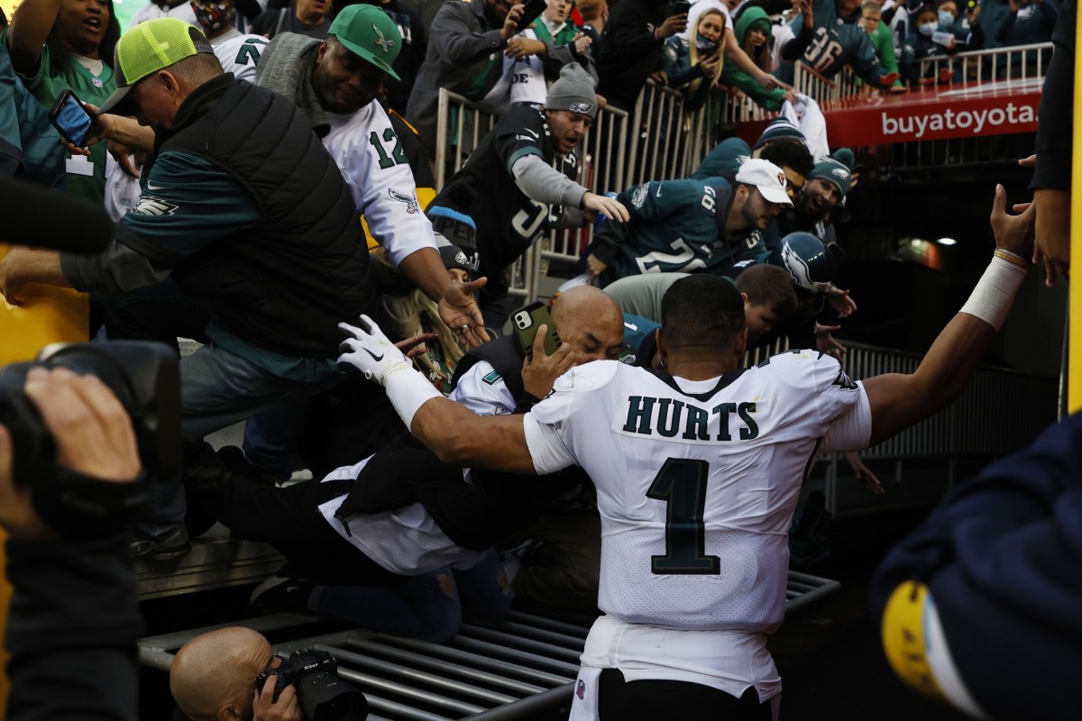 Jalen Hurts walks past fans who are tumbling to the ground when a railing collapsed after the Eagles 20-16 win over Washington