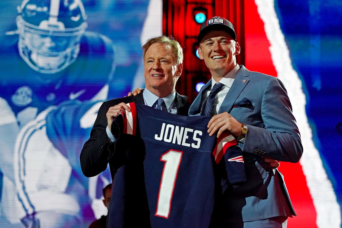 Mac Jones smiles while posing with Roger Goodell, holding up his Patriots jersey, at the 2021 NFL draft