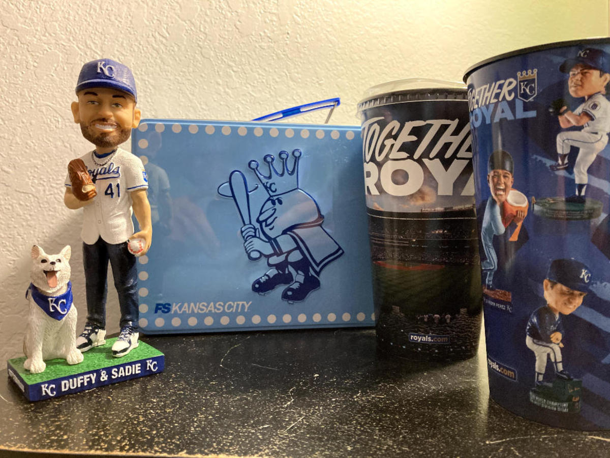 A picture of my early collection, taken just after I brought home my first bobblehead (the Duffy & Sadie bobblehead from 2019) and the Mr. Royal lunchbox. I got the bobblehead cup (right) during my first visit to Kauffman Stadium for my 22nd birthday. I'm two bobbleheads away from owning each bobblehead featured on the cup. (Garrett Fuller)