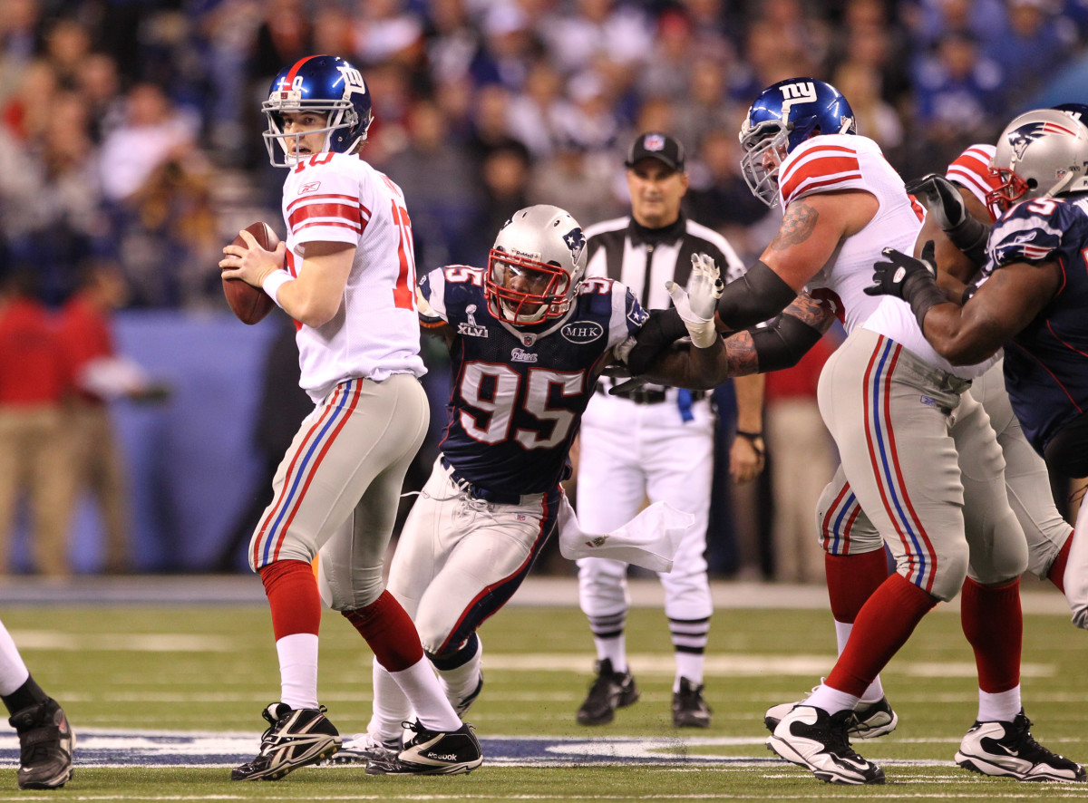 New York Giants quarterback Eli Manning throws in the pocket during the first half with pressure from New England Patriots defensive end Mark Anderson (95) in Super Bowl XLVI at Lucas Oil Stadium.