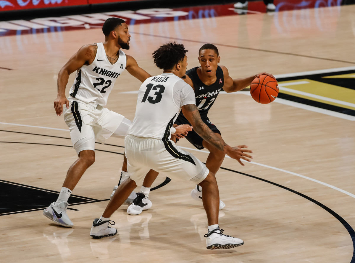 Dec 22, 2020; Orlando, Florida, USA; Cincinnati Bearcats guard Mika Adams-Woods (23) moves the ball against UCF Knights guard Brandon Mahan (13) and UCF Knights guard Darin Green Jr. (22) during the second half at Addition Financial Arena. Mandatory Credit: Mike Watters-USA TODAY Sports