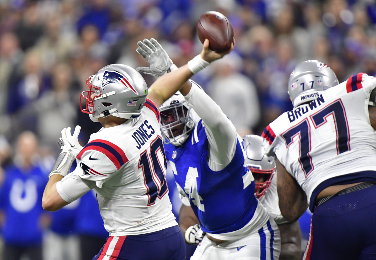 Dec 18, 2021; Indianapolis, Indiana, USA; New England Patriots quarterback Mac Jones (10) gets the ball past Indianapolis Colts defensive end Dayo Odeyingbo (54) during the second half at Lucas Oil Stadium. Colts won 27-17.