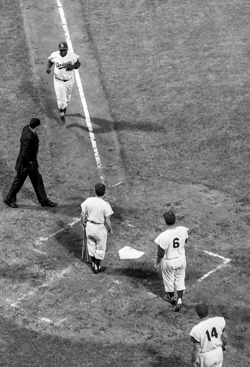 Brooklyn Dodgers second baseman Jackie Robinson (42) approaches his teammates, right fielder Carl Furillo (6) and first baseman Gil Hodges (14), and home plate umpire Bill Engeln while jogging to home plate for an attempt at-bat against the Milwaukee Braves on Thursday, August 2, 1956, in Brooklyn, N.Y. Brooklyn defeated Milwaukee, 3-0.