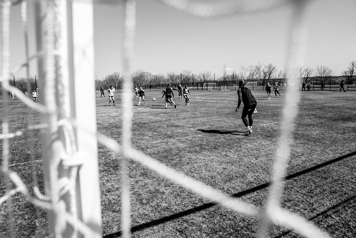 A black-and-white photo of the Washington Spirit practicing, as seen through a soccer net