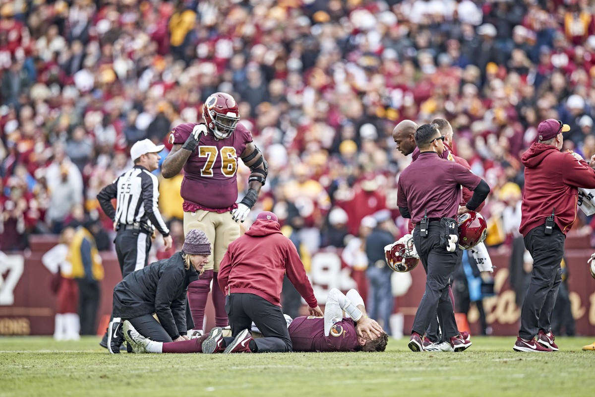 Alex Smith lies on the field with his hands over his face after breaking his right leg during a 2018 game