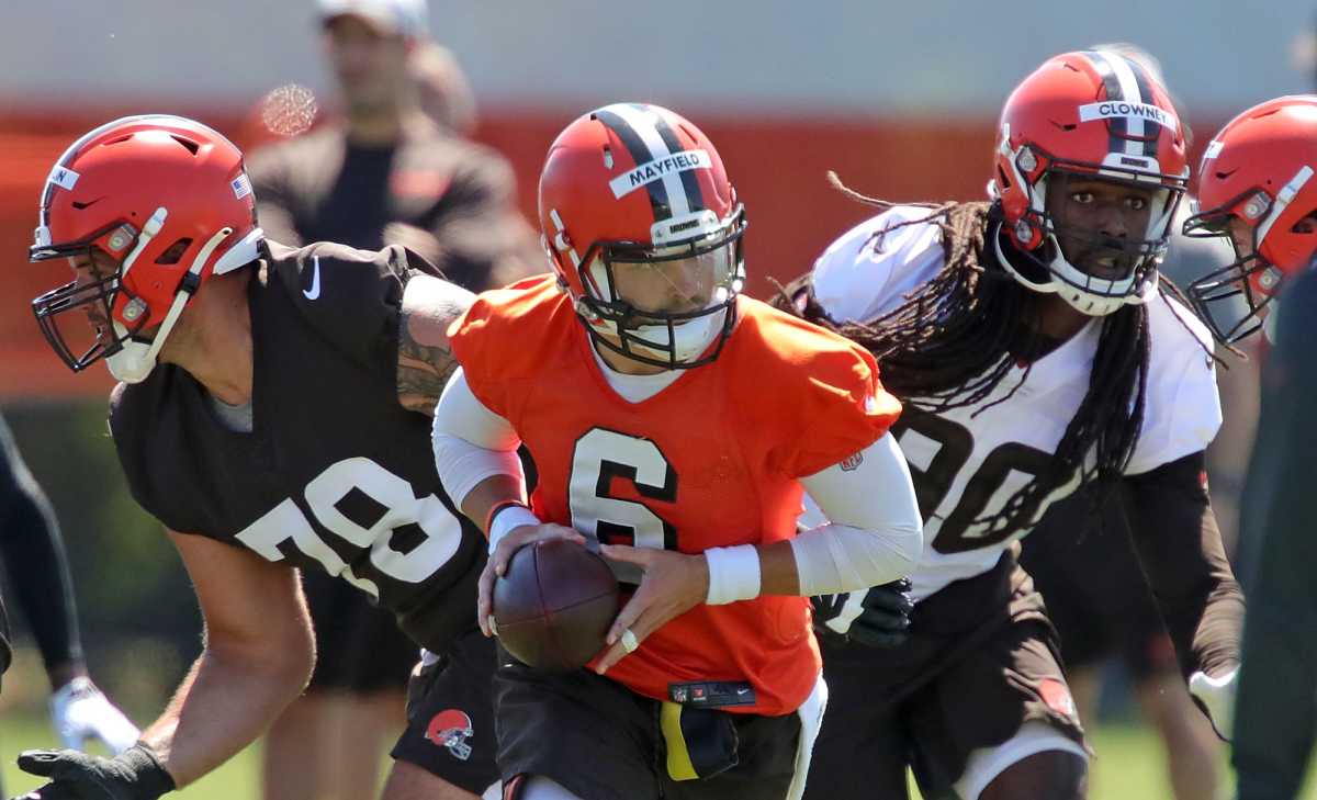 Cleveland Browns quarterback Baker Mayfield (6) looks to make a hand off to a running back under pressure from defensive end Jadeveon Clowney during an NFL football practice at the team's training facility, Wednesday, June 16, 2021, in Berea, Ohio.