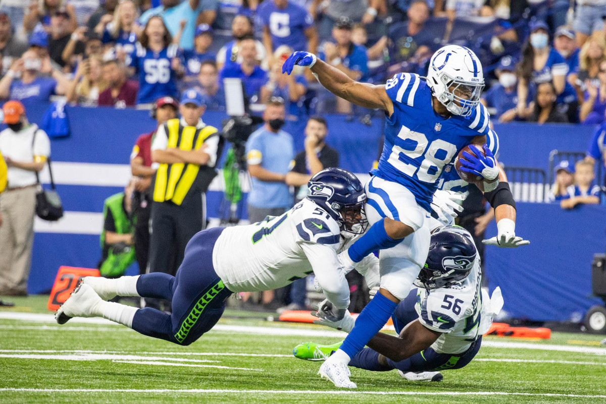 Sep 12, 2021; Indianapolis, Indiana, USA; Indianapolis Colts running back Jonathan Taylor (28) runs the ball while Seattle Seahawks defensive end Kerry Hyder (51) and linebacker Jordyn Brooks (56) defend in the first quarter at Lucas Oil Stadium.