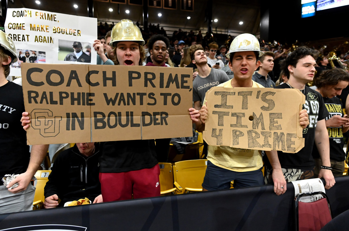Colorado fans at a basketball game hold up signs of support for Deion Sanders.